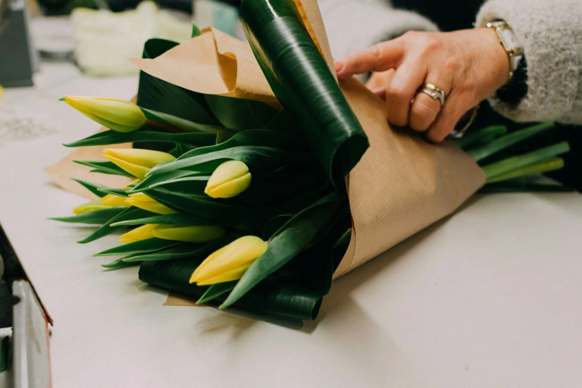 De handen van een bloemist die bruin papier om een bos gele tulpen vouwt