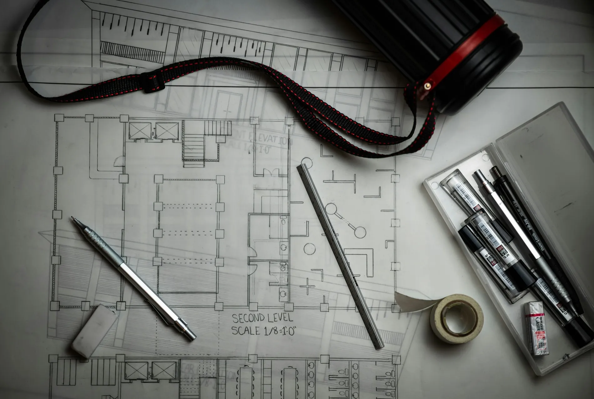 Een plattegrond op een tekentafel met technische pennen, een schaallineaal en een tekenkoker