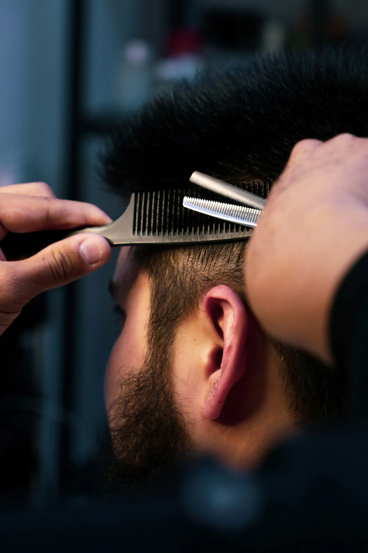 A barber's hands holding a comb and shears against the back of a client's head