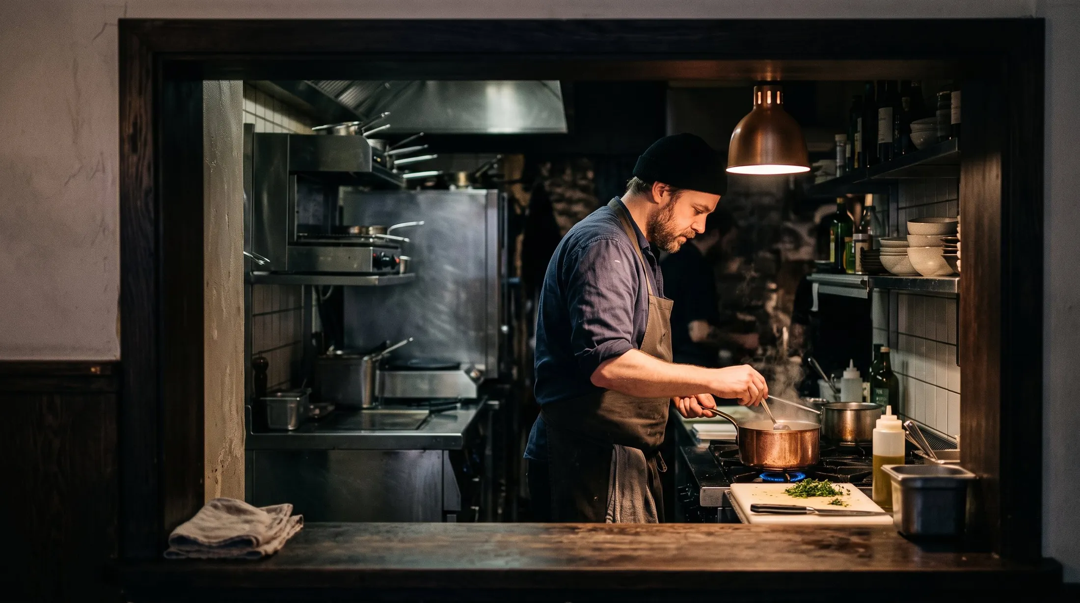 A cook at the stove of a city bistro, seen through the service pass