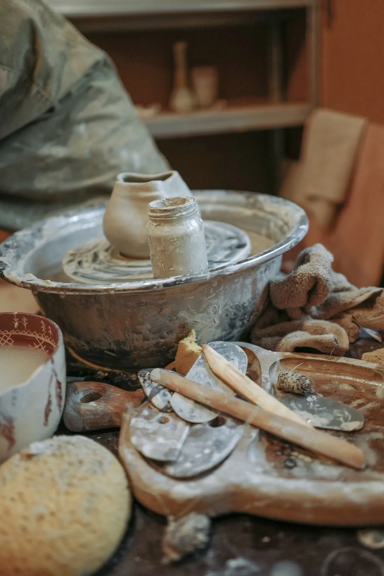 A potter's wheel head surrounded by finished cups, ribs, sponges and wooden tools
