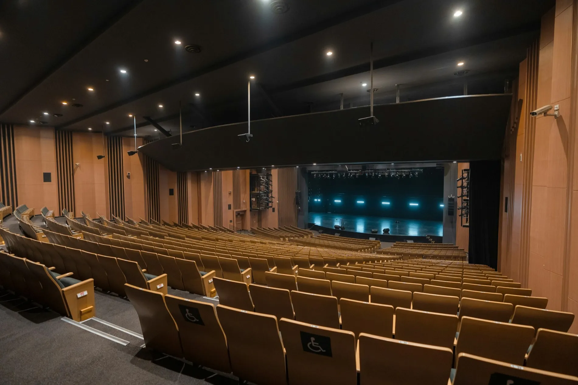 An empty auditorium of pale wooden seats angled toward a lit stage