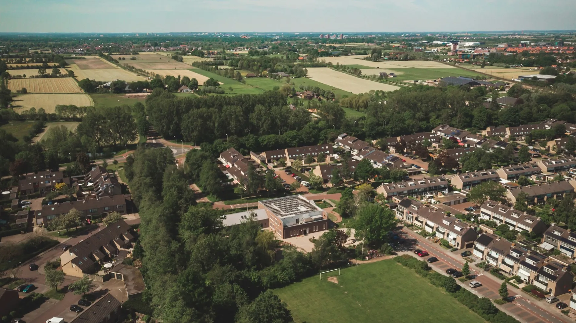 Luchtfoto van een Nederlandse woonwijk met rijen grondgebonden eengezinswoningen, aan de rand van open akkerland.