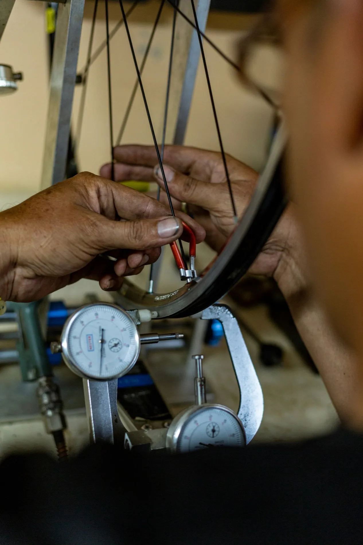 Hands truing a bicycle wheel on a jig, two dial gauges reading against the rim