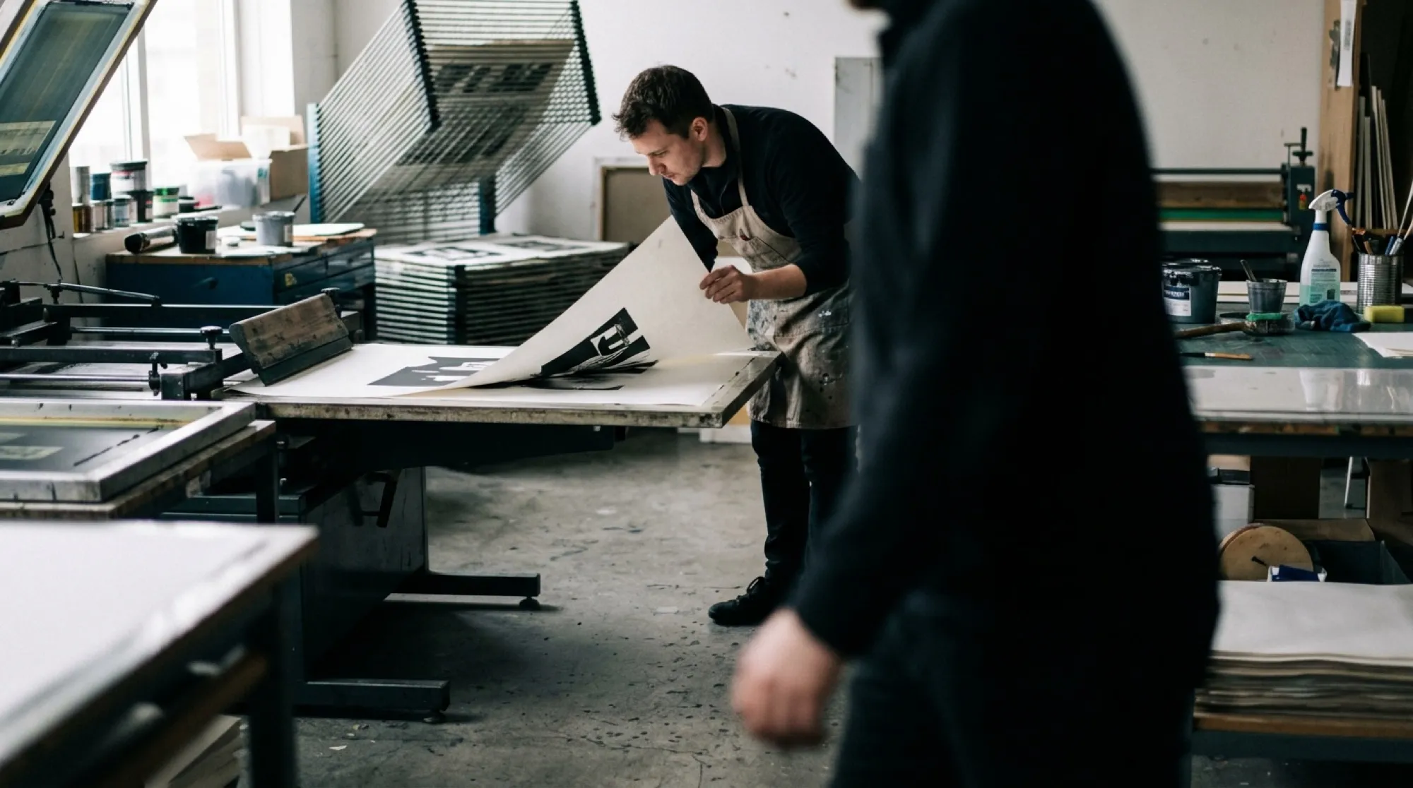 A printmaker reading a freshly pulled sheet in a screen-printing workshop