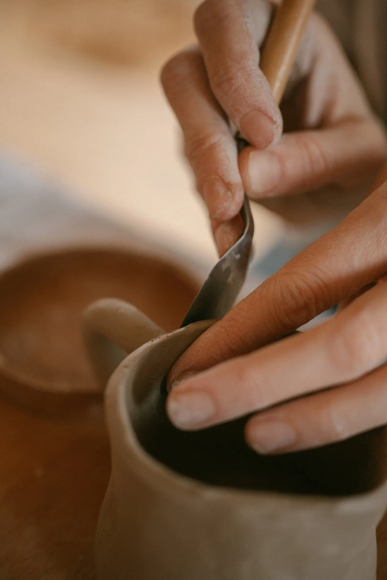 A potter's hands trimming the foot of a bowl with a steel rib as the wheel turns